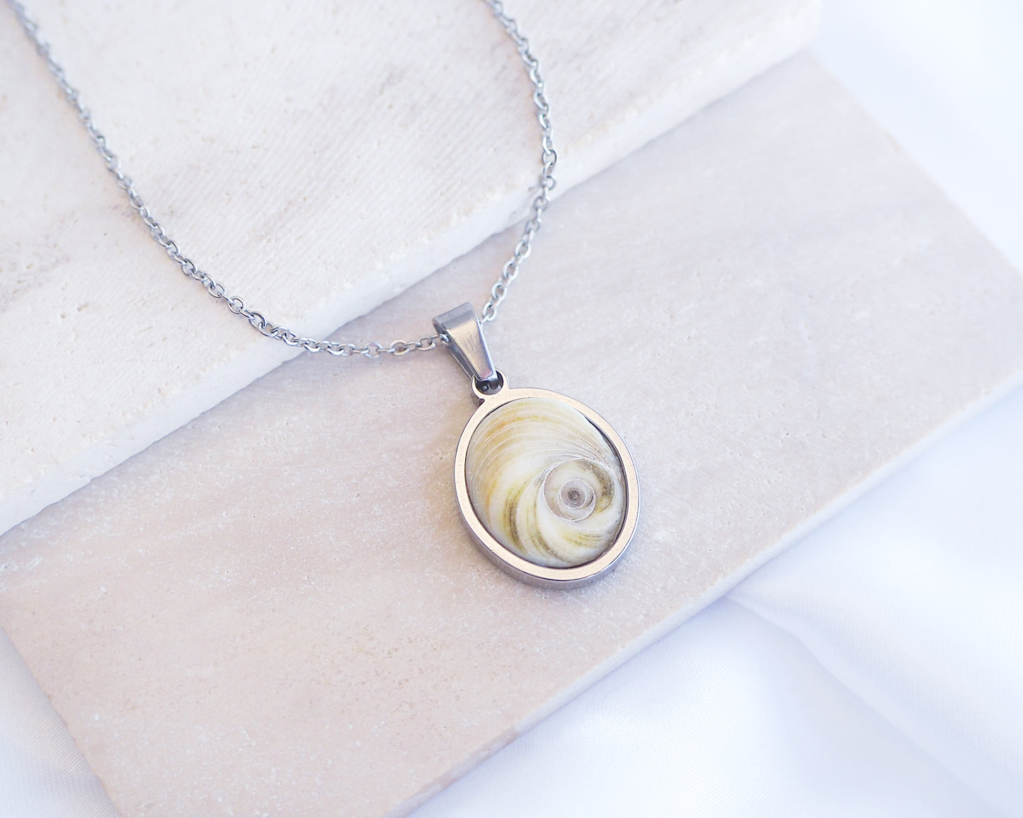 Light Eye of Saint Lucia Silver Necklace front view displayed on stone, silver stainless steel shiva eye pendant necklace, Saint Lucy Eye, operculum pendant