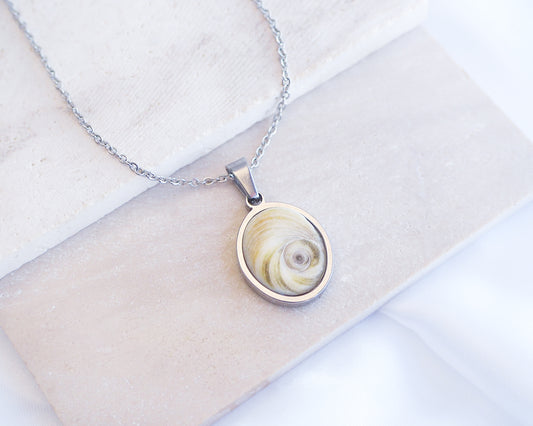 Light Eye of Saint Lucia Silver Necklace front view displayed on stone, silver stainless steel shiva eye pendant necklace, Saint Lucy Eye, operculum pendant