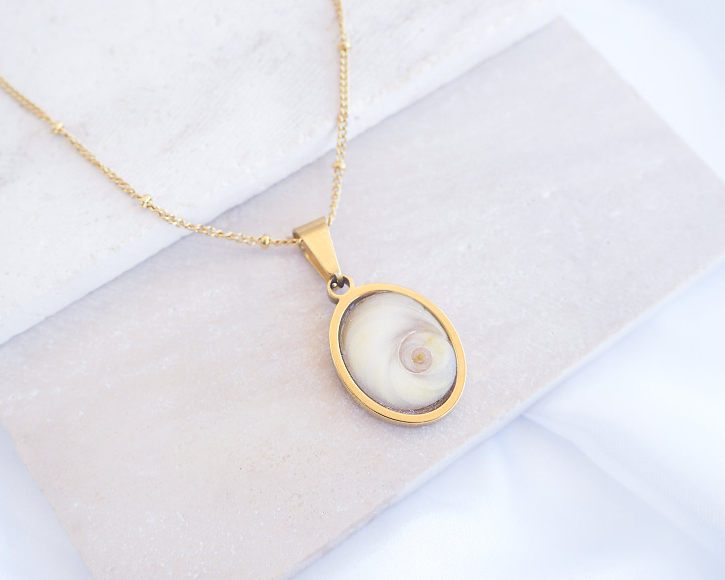 Ivory White Eye of Saint Lucia Gold Necklace on stone displayed, 18k gold stainless steel shiva eye pendant necklace, Saint Lucy Eye, operculum pendant