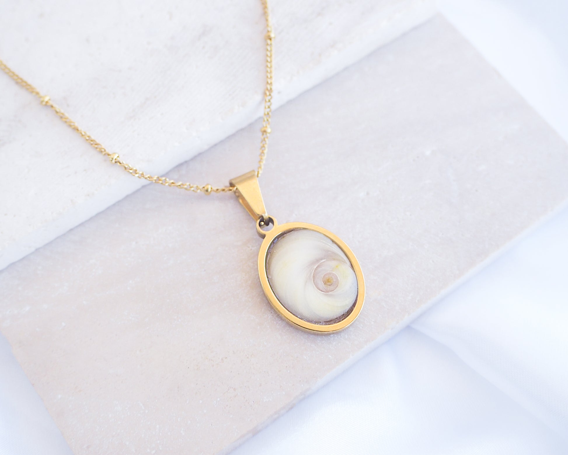 Ivory White Eye of Saint Lucia Gold Necklace on stone displayed, 18k gold stainless steel shiva eye pendant necklace, Saint Lucy Eye, operculum pendant