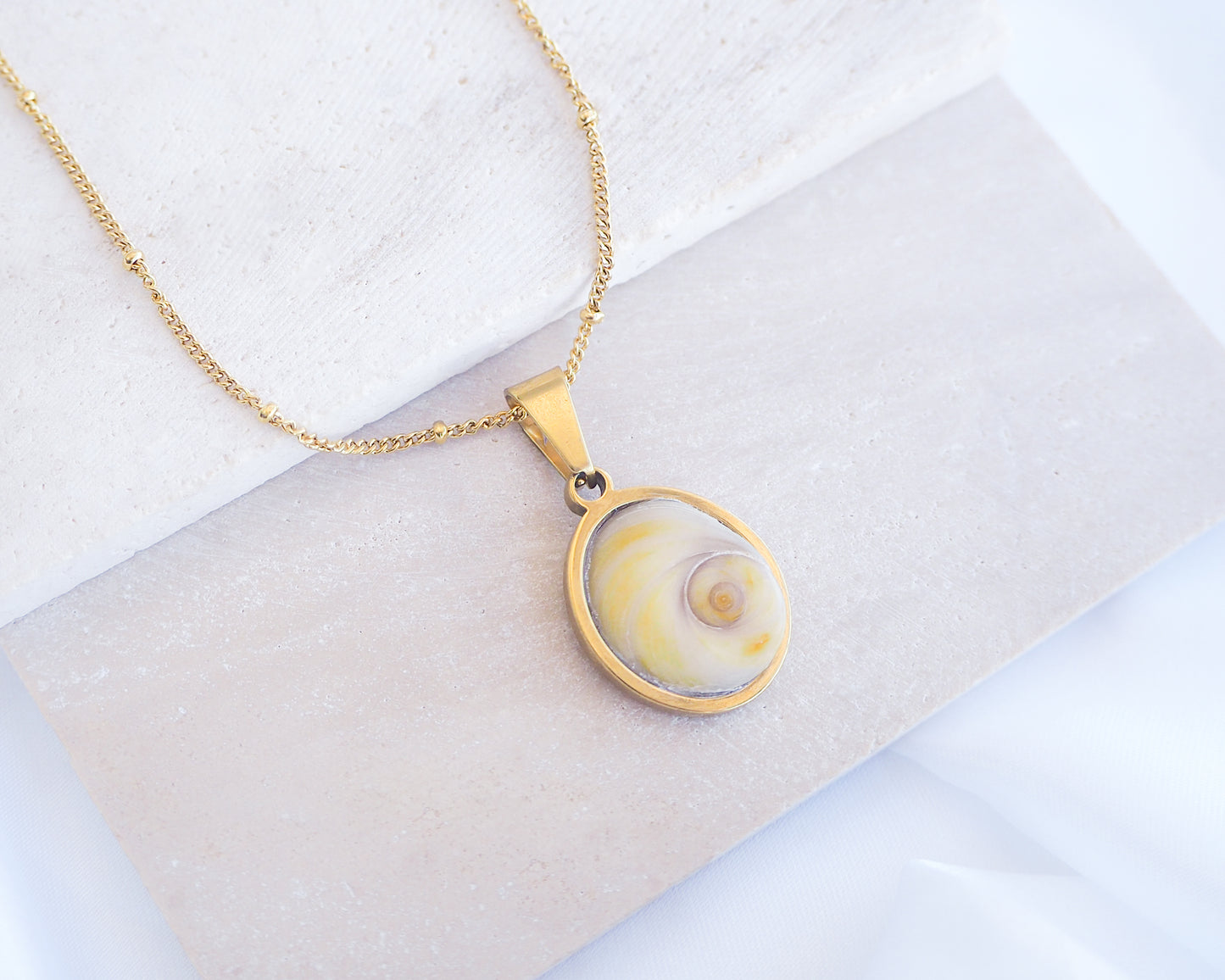 Soft Yellow Shiva Eye Necklace III on stone displayed. Light Eye of Saint handpicked from Portugal, 18k gold stainless steel shiva eye pendant necklace, Saint Lucy Eye, operculum pendant