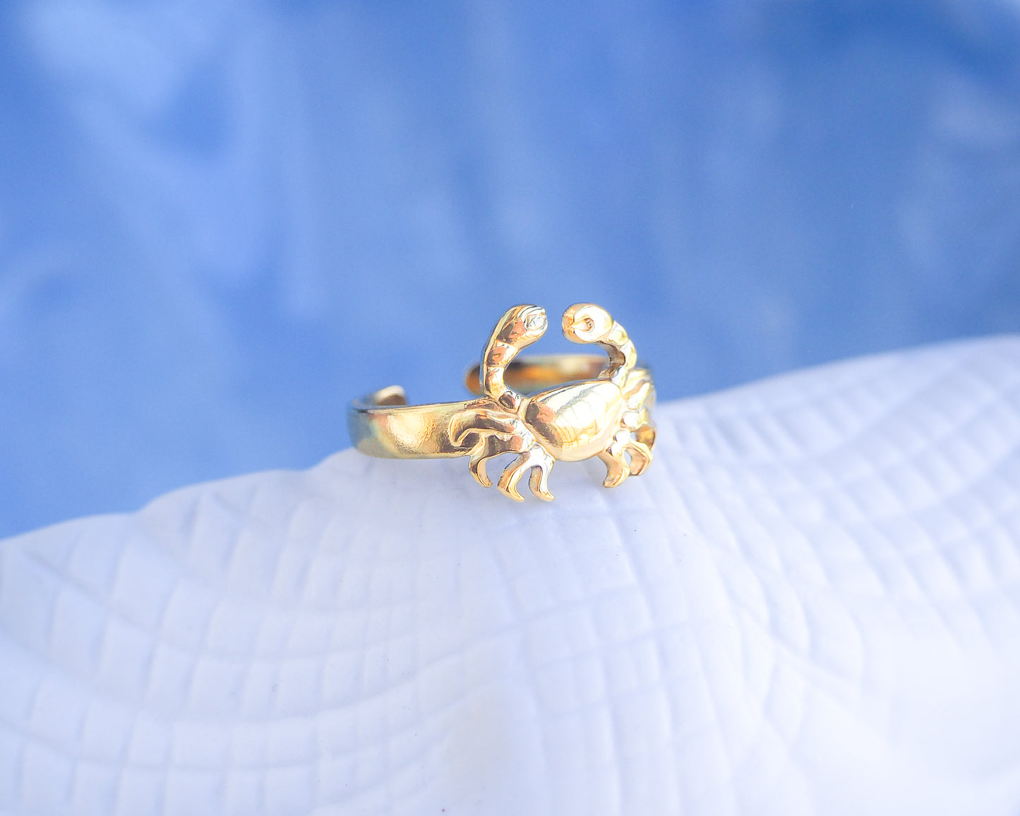 Gold crab-shaped ring on a textured surface with a blue gradient background. Gold Cancer Zodiac Ring with blue white background displayed, adjustable 18k gold stainless steel crab ring 