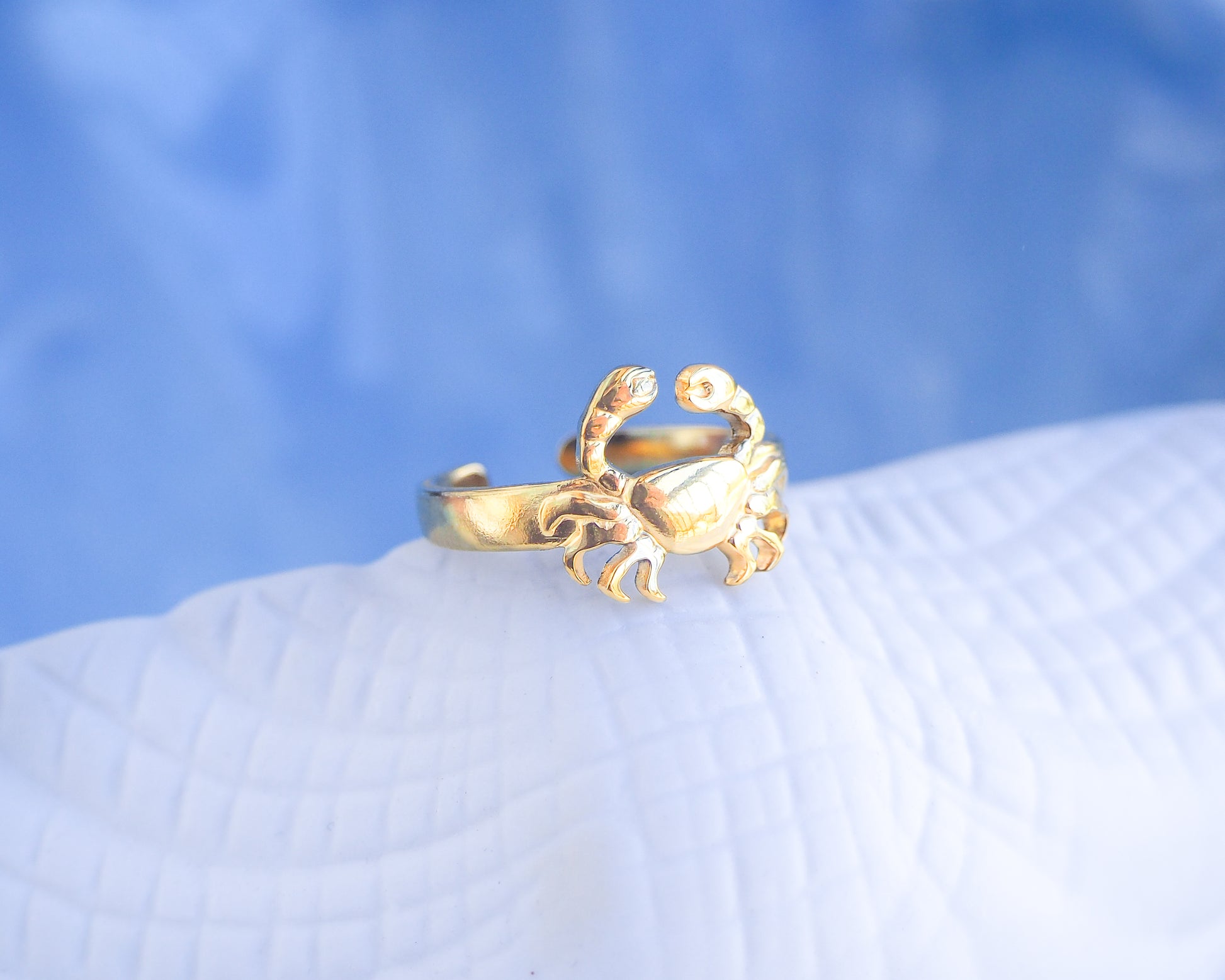 Gold crab-shaped ring on a textured surface with a blue gradient background. Gold Cancer Zodiac Ring with blue white background displayed, adjustable 18k gold stainless steel crab ring 
