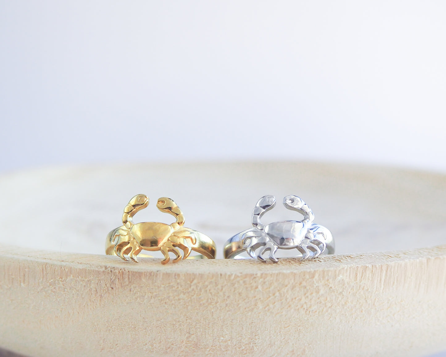 Gold and silver crab-shaped rings on a wooden surface with a white background