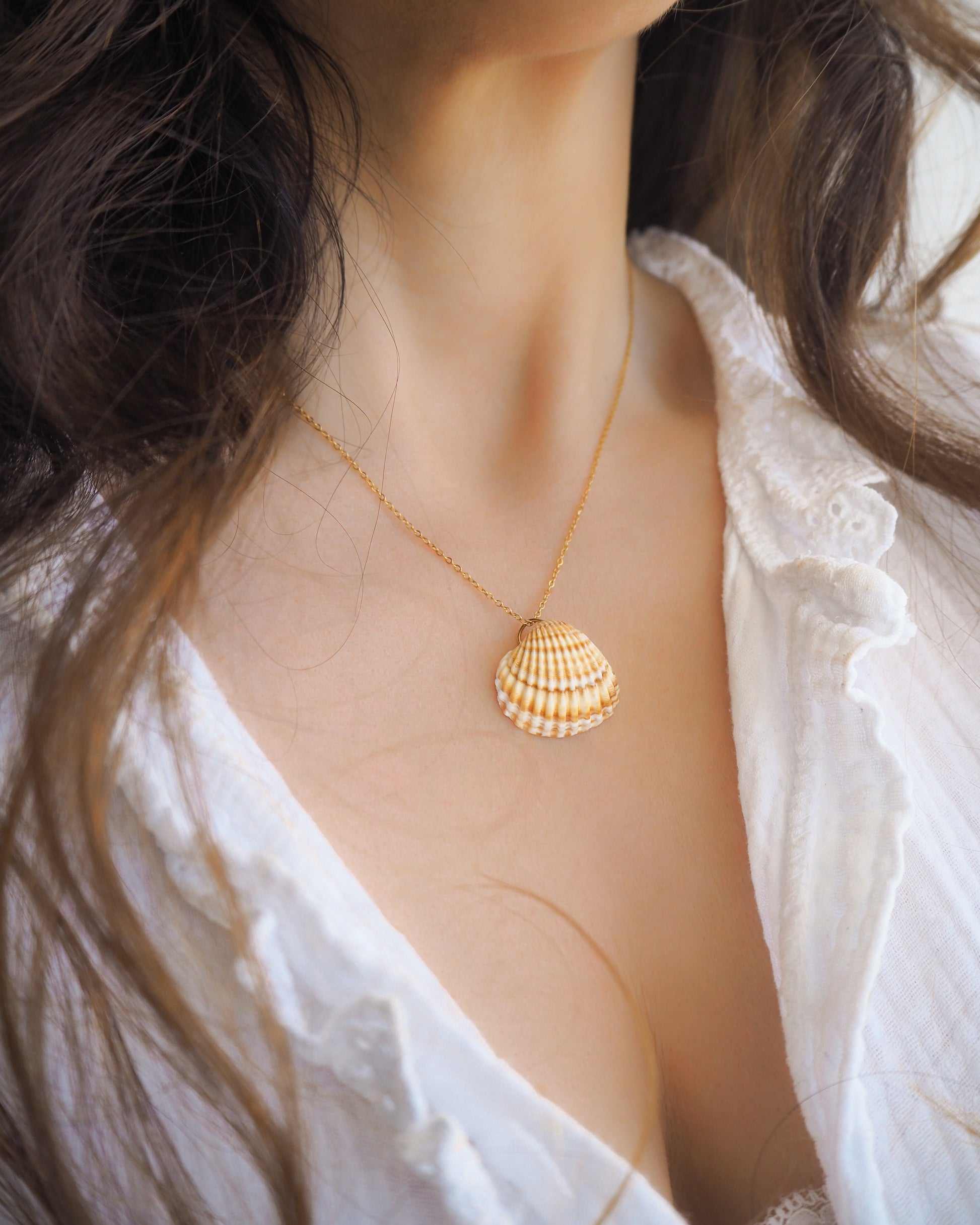 Model wearing a gold cockle shell necklace made with a Mediterranean Cockle Shell from Portugal on a 18k gold stainless steel chain against on neck. The shell is yellow with white stripes.