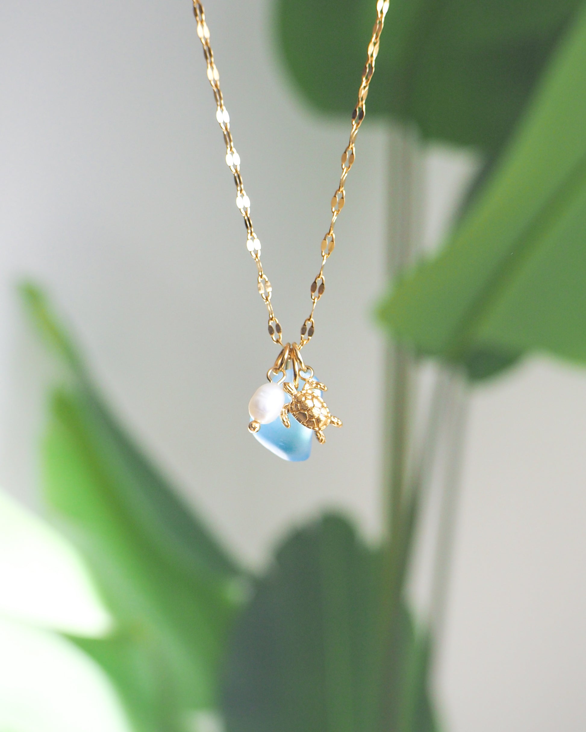 Gold necklace with a blue pendant against a green leafy background