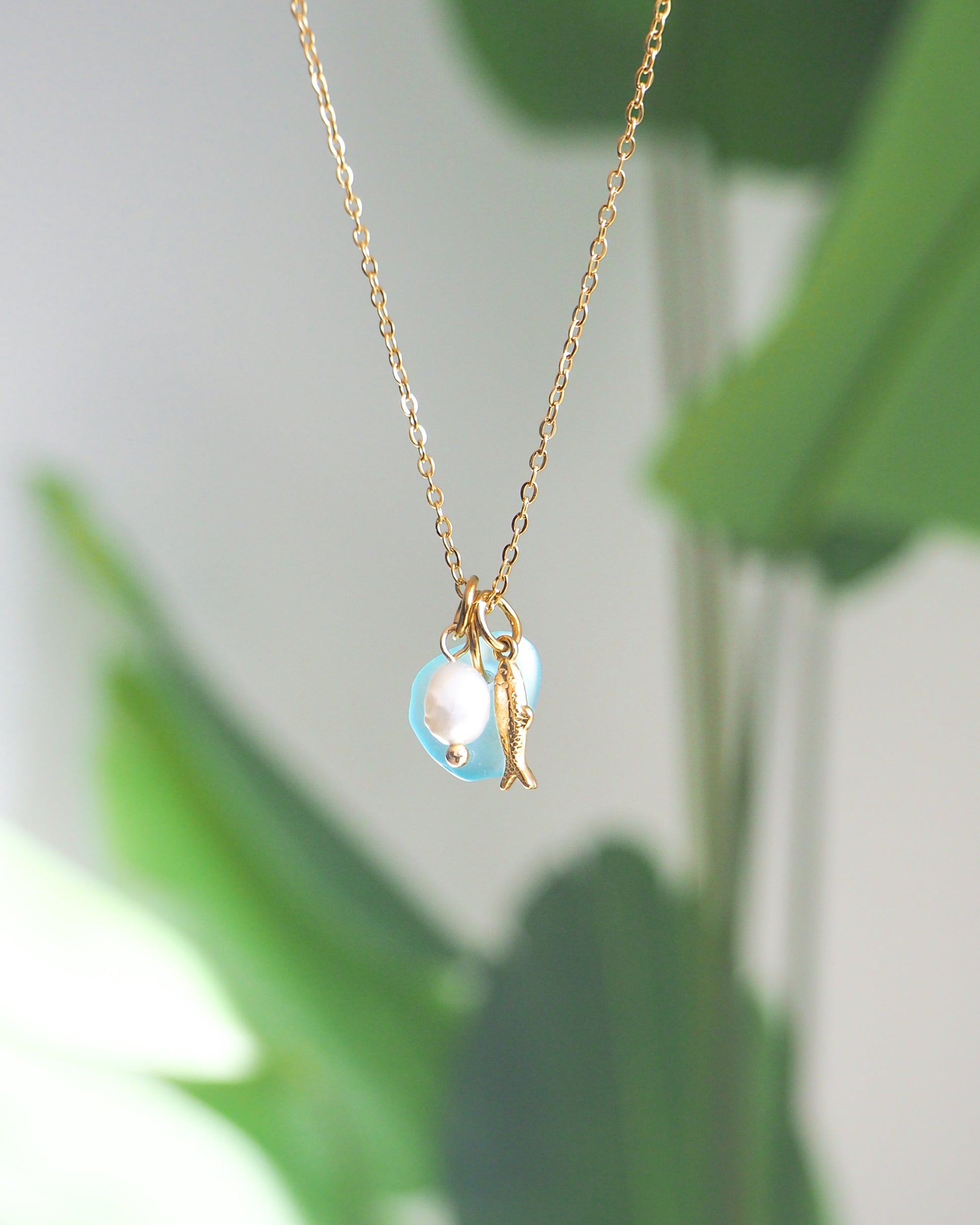Gold necklace with a pearl pendant against a blurred green leaf background
