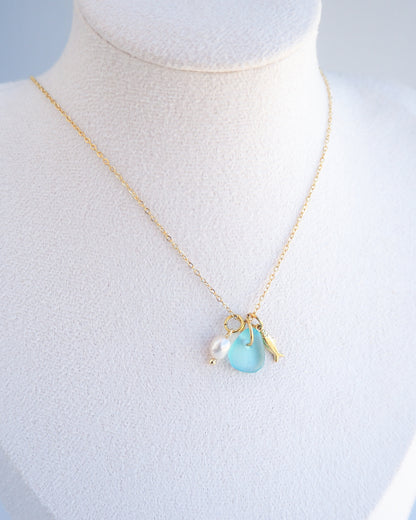 Close up of a necklace with a tiny sardine fish pendant, turquoise blue sea glass and freshwater pearl pendant on display. Made with gold stainless steel chain.