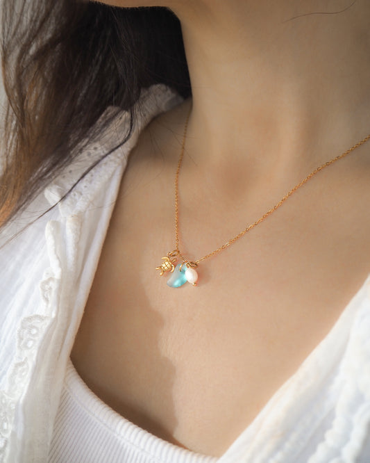 Model wearing Tiny Sea Turtle Blue Sea Glass Pearl Necklace on stone displayed, tiny turtle necklace, turquoise blue necklace, coastal jewelry, freshwater pearl necklace, gold turtle necklace 