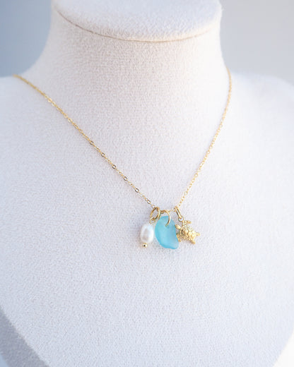 Necklace with a blue pendant and gold chain on a mannequin bust. Tiny Sea Turtle Blue Sea Glass Pearl Necklace on stone displayed, tiny turtle necklace, turquoise blue necklace, coastal jewelry, freshwater pearl necklace, gold turtle necklace 