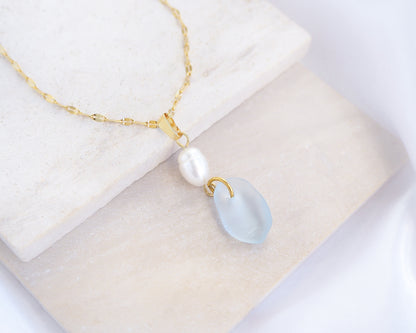 Necklace with a pearl and teardrop blue seaglass pendant on stone displayed., Coastal jewelry with freshwater pearl necklace. Made with light blue sea glass and 18k gold stainless steel. Ocean-inspired jewelry, beach necklace, ocean treasure necklace