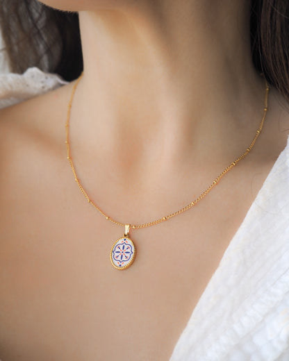 Model wearing a gold Portuguese Tile Oval Necklaces on neck. Made with 18k gold stainless steel and white blue mosaic pendant inspired by the Portuguese Azulejo design pattern. 