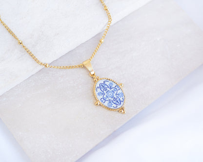 Close up of Blue Portuguese Tile Oval Deluxe Necklaces Blue on stone displayed. Made with 18k gold stainless steel and white blue mosaic pendant inspired by the Portuguese Azulejo design pattern. 