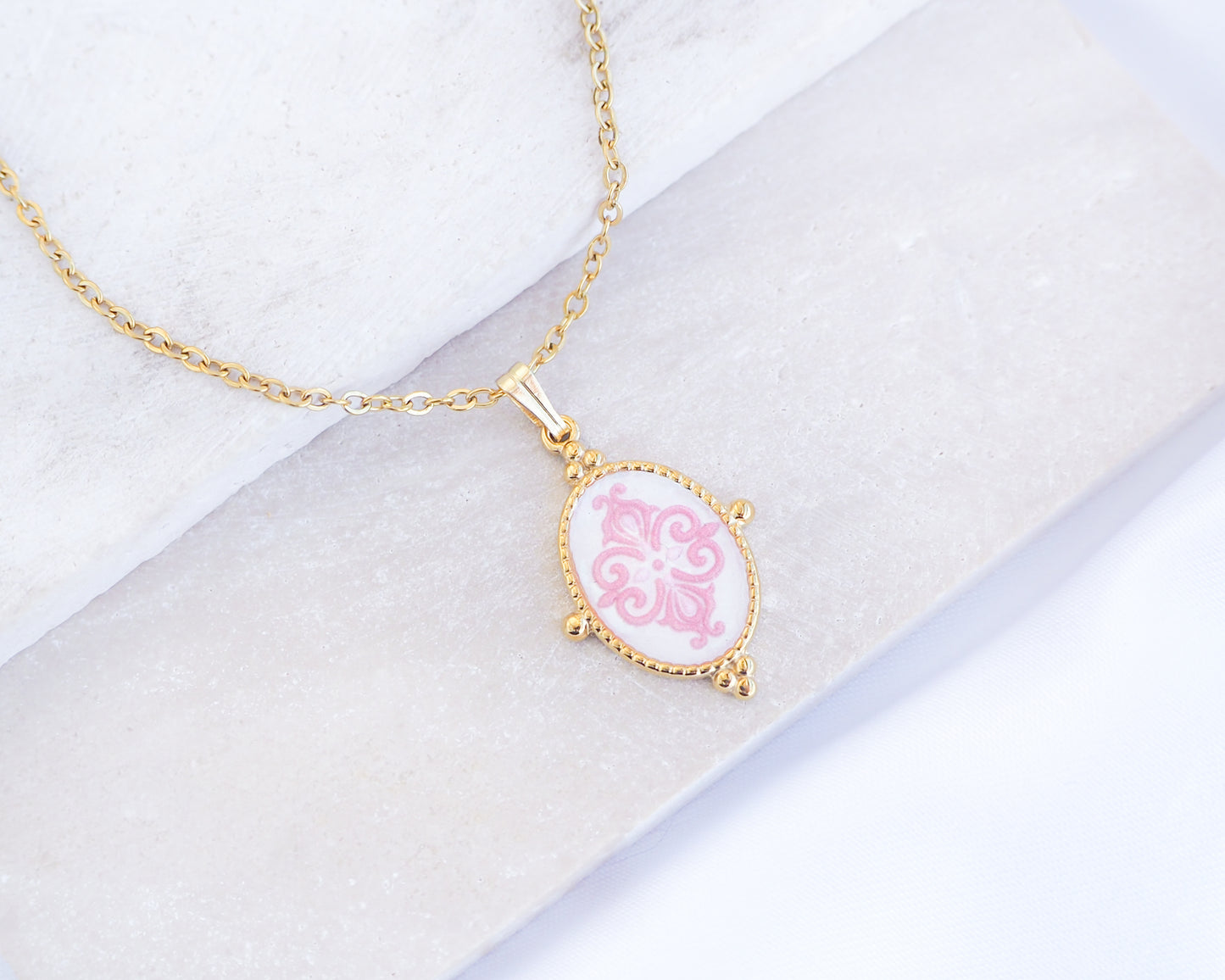 Close up of Pink Portuguese Tile Oval Necklaces Blue on stone displayed. Made with 18k gold stainless steel and white pink mosaic pendant inspired by the Portuguese Azulejo design pattern. 