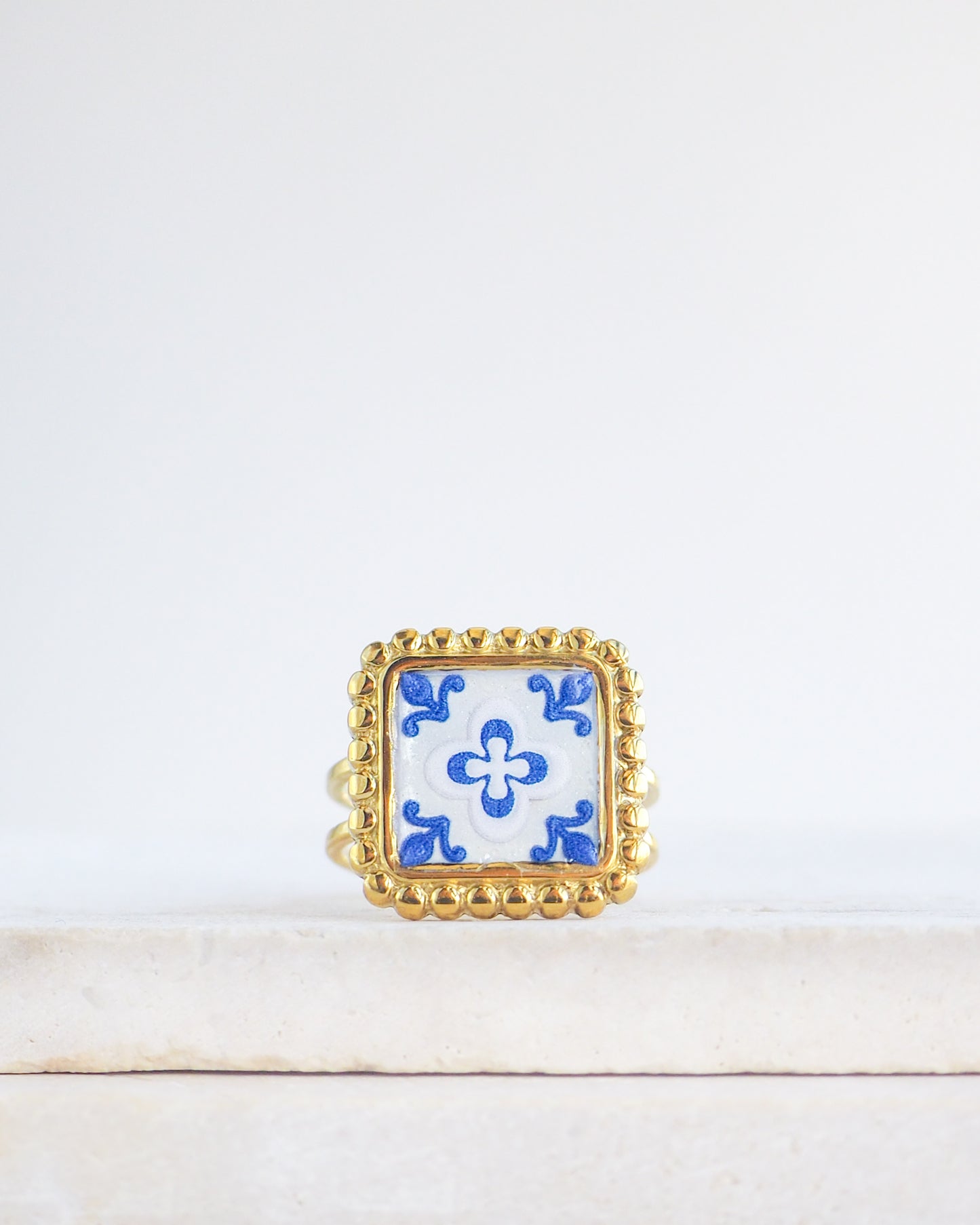Blue White Gold Portuguese Tile Square Ring on stone displayed. Rings is handmade with 18k gold stainless steel and has a blue white floral tile pattern inspired by the Portuguese azulejos tiles. 