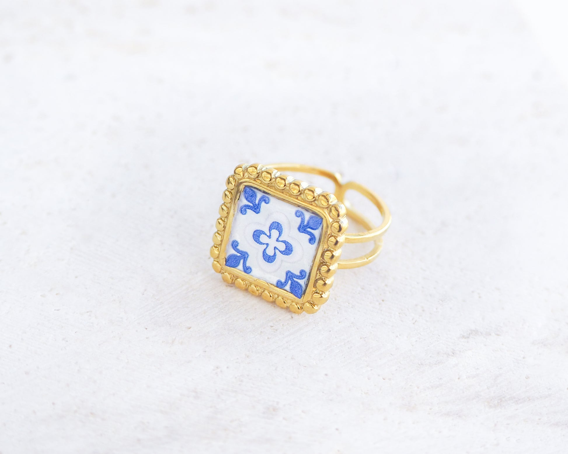 Left view of Blue Gold Portuguese Tile Square Ring on stone displayed. Rings is handmade with 18k gold stainless steel and has a blue white floral tile pattern inspired by the Portuguese azulejos tiles. 