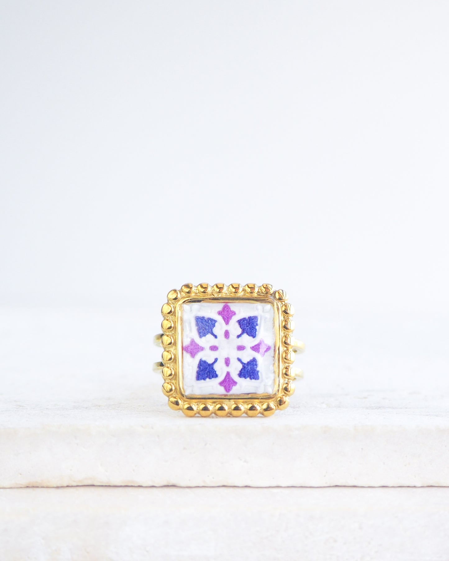 Purple Gold Portuguese Tile Square Ring on stone displayed. Rings is handmade with 18k gold stainless steel and has a purple and pink tile pattern inspired by the Portuguese azulejos tiles. 