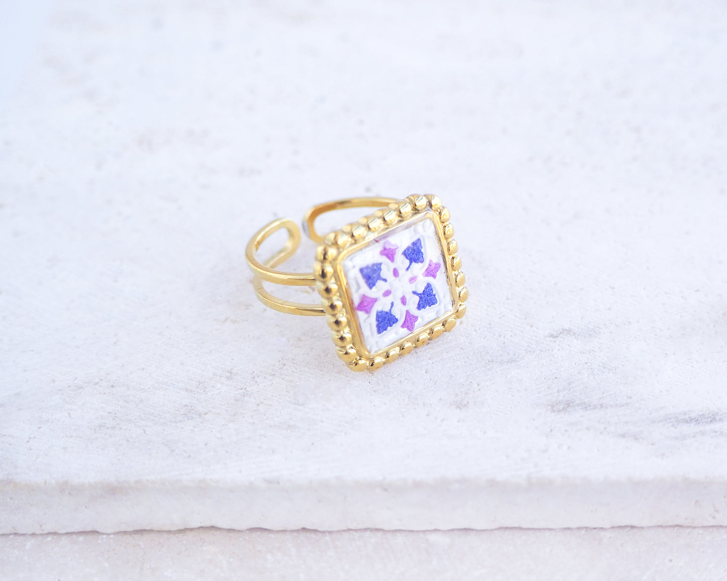 Side view of Purple Gold Portuguese Tile Square Ring on stone displayed. Rings is handmade with 18k gold stainless steel and has a purple pink tile pattern inspired by the Portuguese azulejos tiles. 