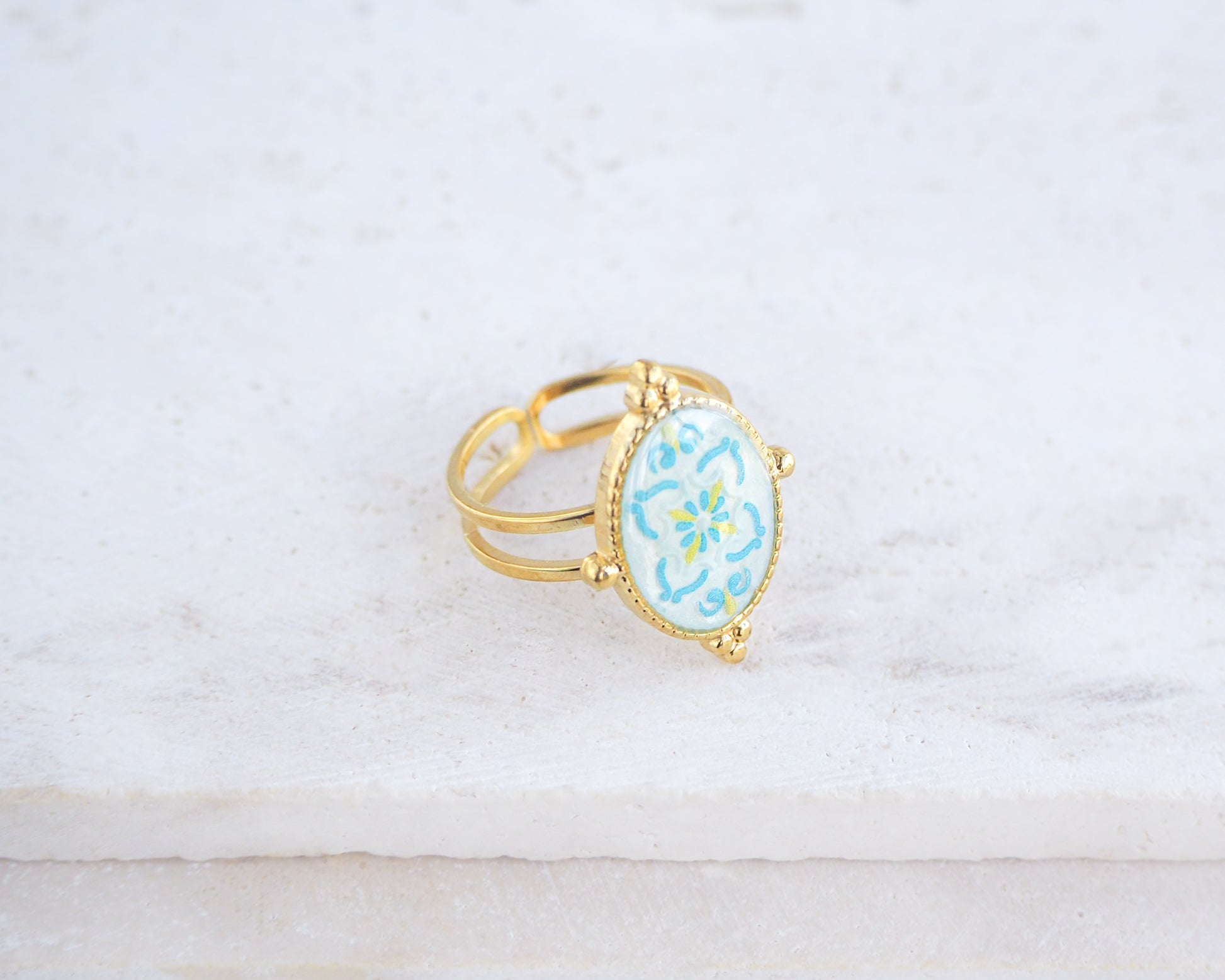 Left view of Blue Turquoise Portuguese Tile Oval Deluxe Rings on stone displayed. The ring is handmade with 18k gold stainless steel and are made with different patterns inspired by the Portuguese azulejos tiles. 