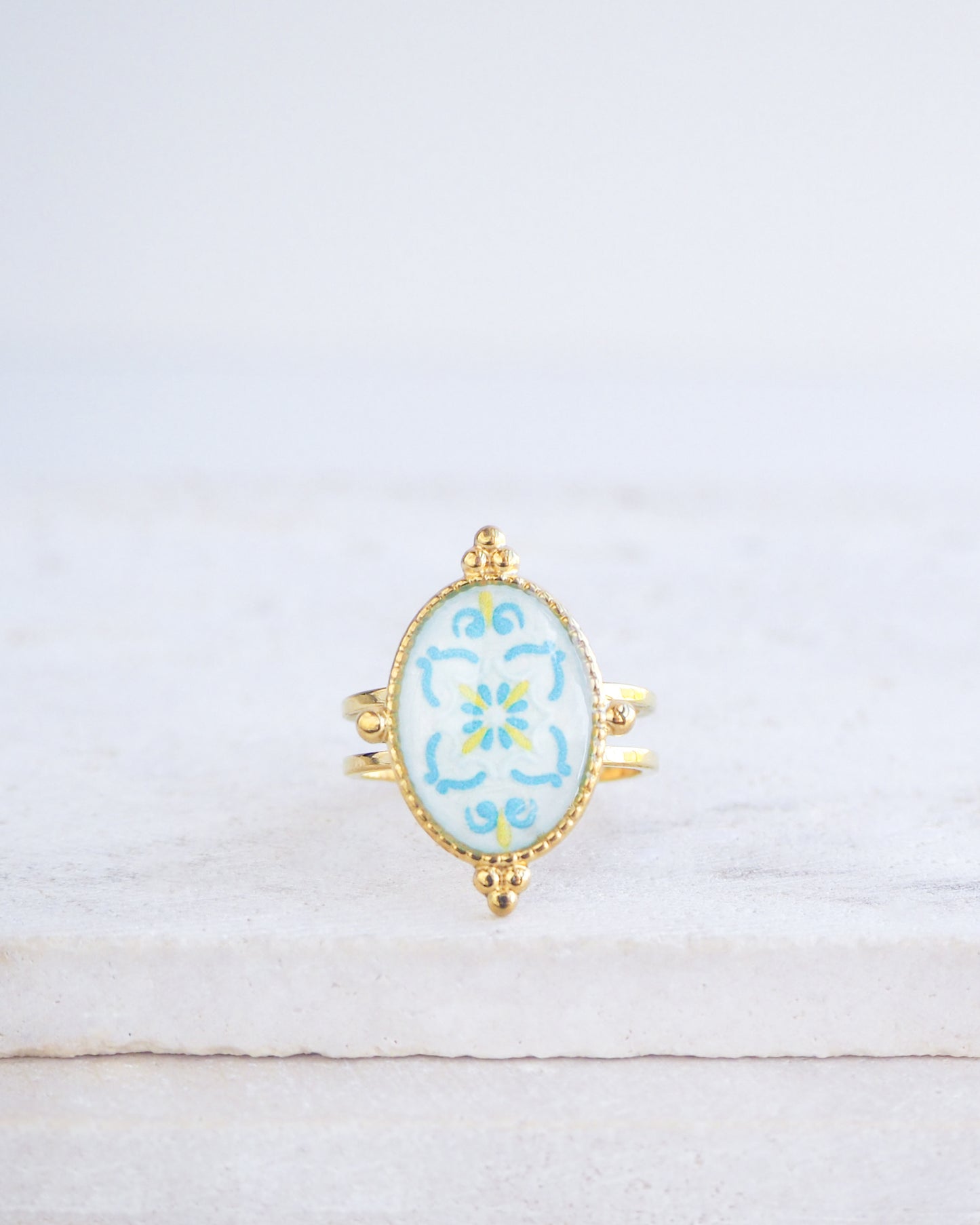 Blue Turquoise Portuguese Tile Oval Deluxe Rings on stone displayed. The ring is handmade with 18k gold stainless steel and are made with different patterns inspired by the Portuguese azulejos tiles. 