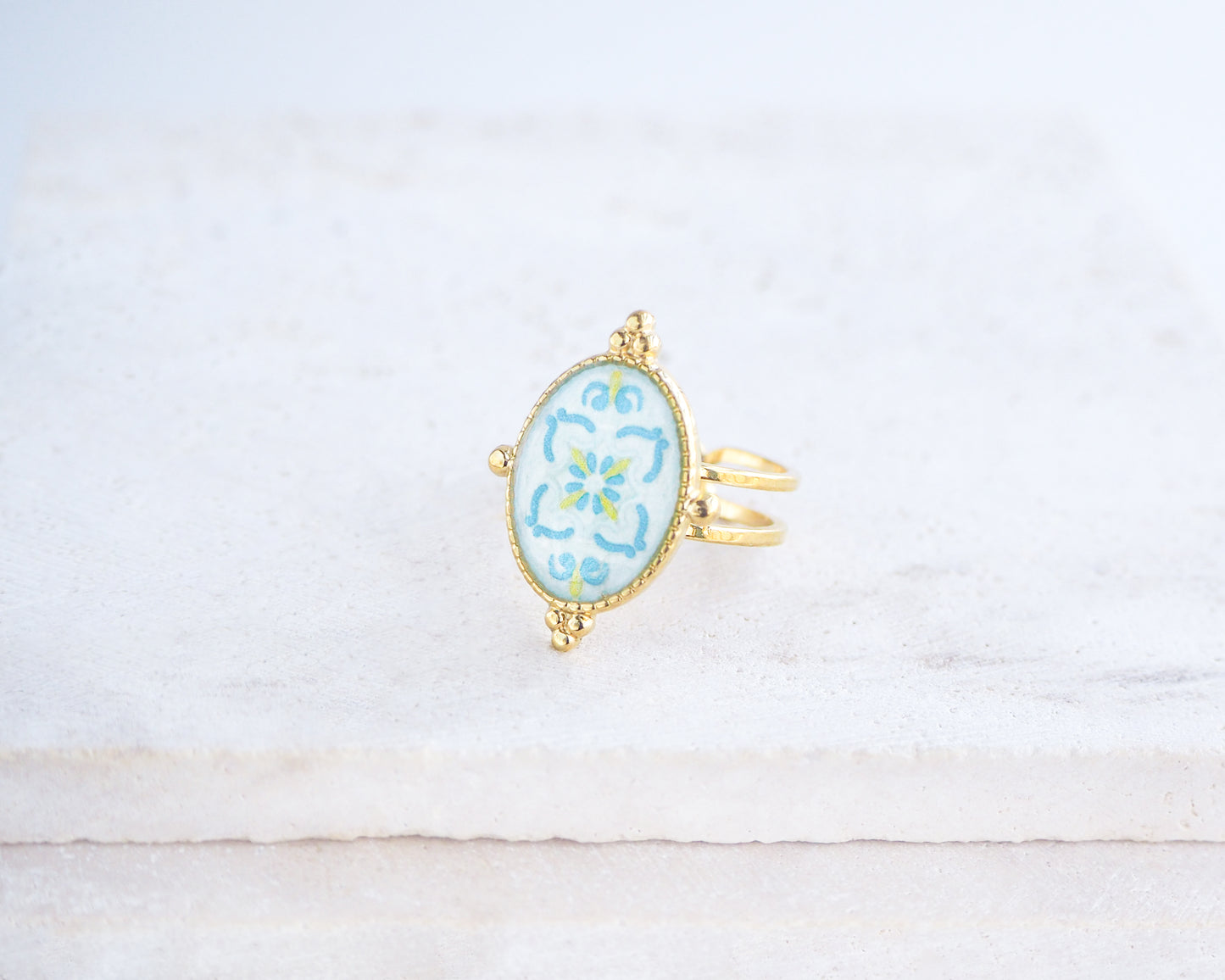 side view of Blue Turquoise Portuguese Tile Oval Deluxe Rings on stone displayed. The ring is handmade with 18k gold stainless steel and are made with different patterns inspired by the Portuguese azulejos tiles. 