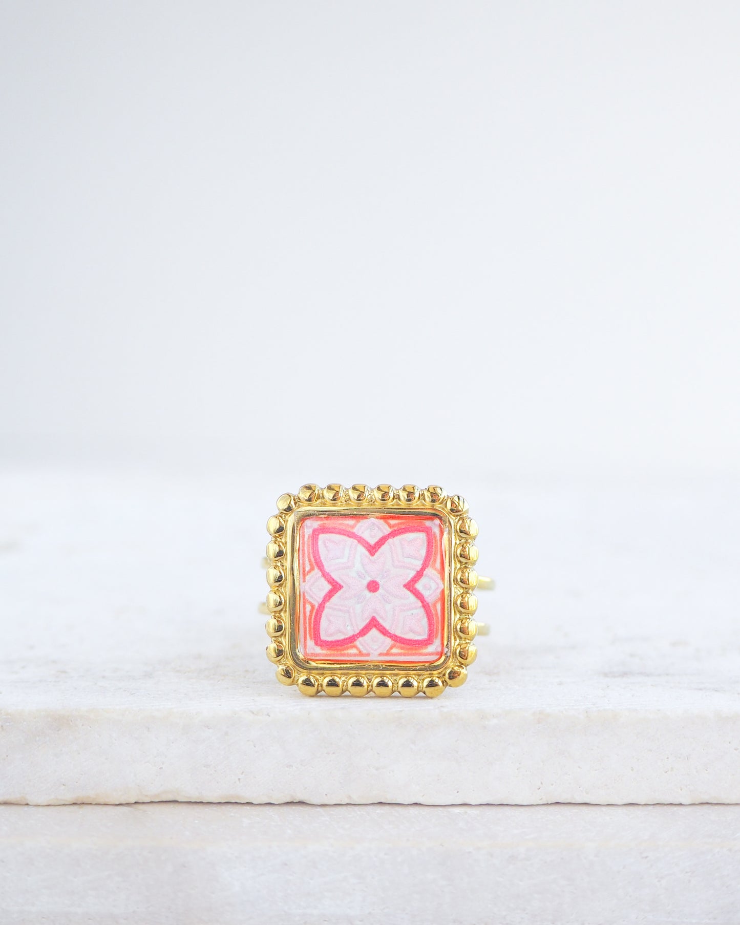 Pink orange Gold Portuguese Tile Square Ring on stone displayed. Rings is handmade with 18k gold stainless steel and has a pink orange floral tile pattern inspired by the Portuguese azulejos tiles. 