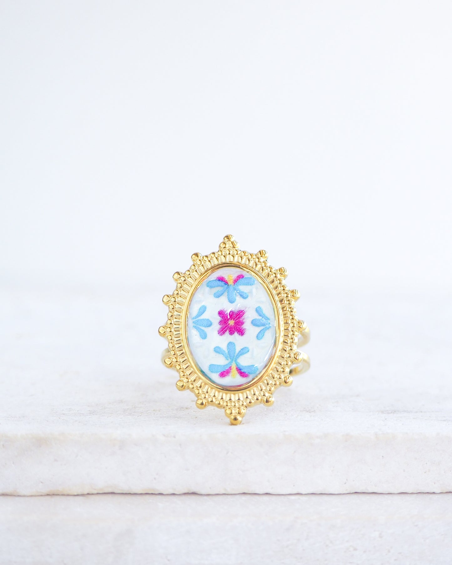 Front view of Blue Fuchsia Portuguese Tile Oval Deluxe Rings on stone displayed. The ring is handmade with 18k gold stainless steel and are made with different patterns inspired by the Portuguese azulejos tiles. 