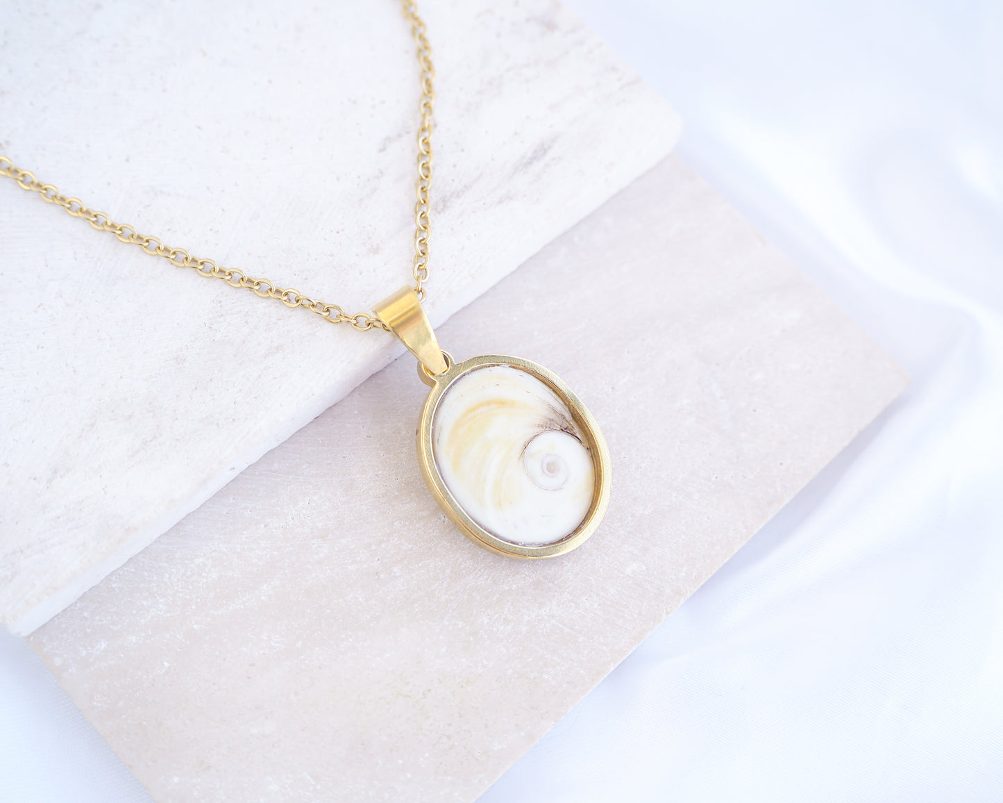 White Eye of Saint Lucia Gold Necklace II on stone displayed, 18k gold stainless steel shiva eye pendant necklace, Saint Lucy Eye, operculum pendant