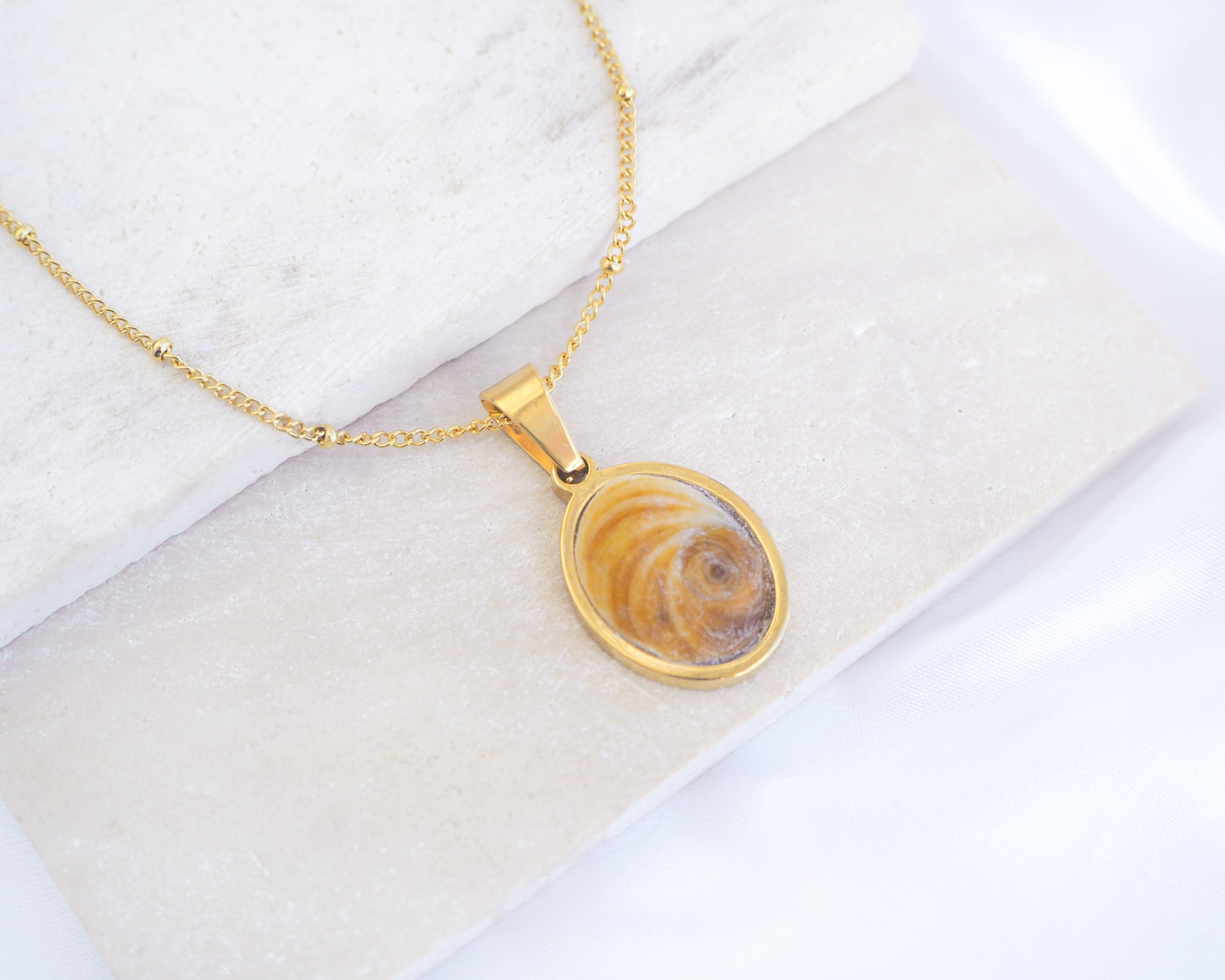 Brown Orange Eye of Saint Lucia Gold Necklace on stone displayed, 18k gold stainless steel brown shiva eye pendant necklace, Saint Lucy Eye, operculum pendant