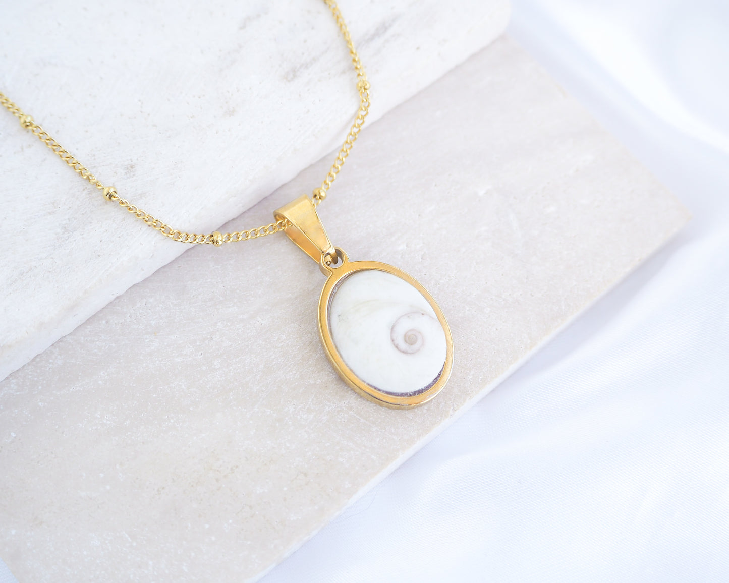 White Eye of Saint Lucia Gold Necklace III on stone displayed, 18k gold stainless steel shiva eye pendant dot chain necklace, Saint Lucy Eye, operculum pendant