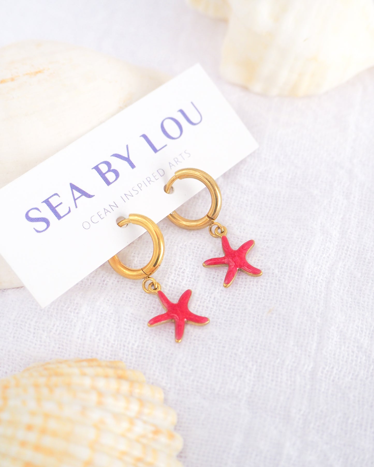 Tiny starfish hoop earrings displayed on white Sea by Lou jewelry card. The starfish pendants are red. Made with 18k gold stainless steel earring hoops. Beach jewelry for summer days. Minimalistic coastal earrings. Perfect to mix and match with other earrings.