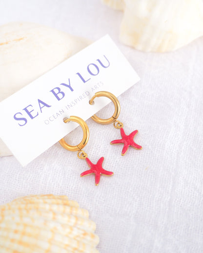 Tiny starfish hoop earrings displayed on white Sea by Lou jewelry card. The starfish pendants are red. Made with 18k gold stainless steel earring hoops. Beach jewelry for summer days. Minimalistic coastal earrings. Perfect to mix and match with other earrings.