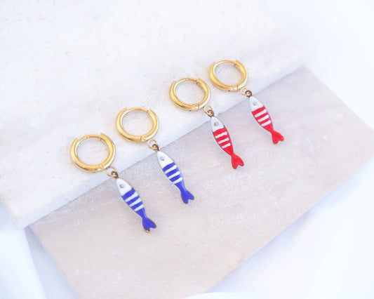 Two pairs of tiny sardine fish hoop earrings displayed on light stone. The fish pendants are red and white striped and blue and white striped. Made with 18k gold stainless steel earring hoops. Beautiful gift for Portugal lovers or holiday memory, coastal jewelry from Portugal. Nautical minimalistic jewelry 