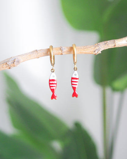 Front view of tiny sardine fish hoop earrings with green plant background. The fish pendant is red and white striped. Made with 18k gold stainless steel earring hoops. Beautiful gift for Portugal lovers or holiday memory, coastal jewelry from Portugal. Nautical minimalistic jewelry 