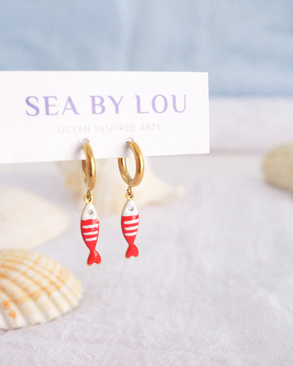 Front view of tiny sardine fish hoop earrings displayed on white Sea by Lou jewelry card. The fish pendant is red and white striped. Made with 18k gold stainless steel earring hoops. Beautiful gift for Portugal lovers or holiday memory, coastal jewelry from Portugal. Nautical minimalistic jewelry 