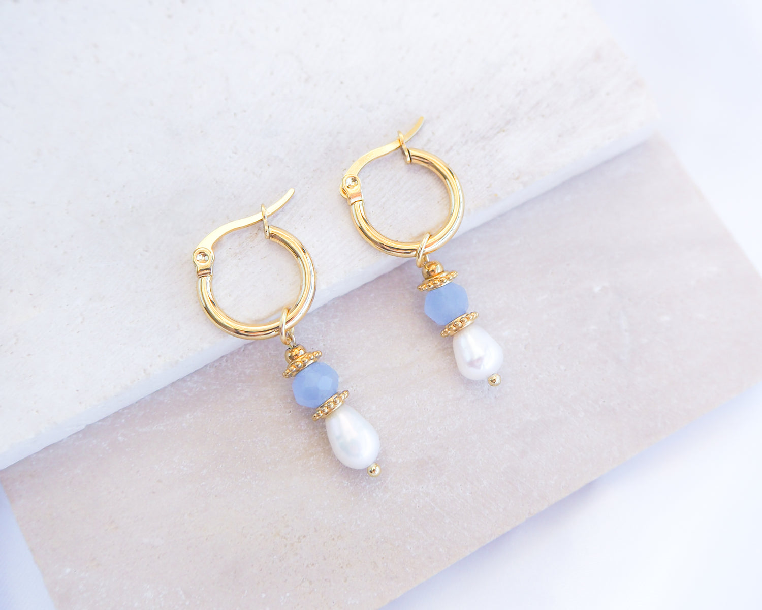 Gold hoop earrings with blue and white beads on a light background. Handmade with blue sparkling crystal beads, ivory freshwater pearls and 18k gold stainless steel beads. These earrings are inspired on the ocean is part of the ocean serenity pearl collection. 