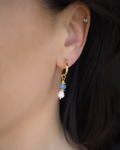 Close-up of an ear wearing a gold hoop earring with blue beads and white freshwater pearls. Handmade with blue sparkling crystal beads, ivory freshwater pearls and 18k gold stainless steel beads. These earrings are inspired on the ocean is part of the ocean serenity pearl collection. 