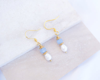 Pair of earrings with gold hooks, blue and white beads on a light background. Handmade with blue sparkling crystal beads, ivory freshwater pearls and 18k gold stainless steel beads. These earrings are inspired on the ocean is part of the ocean serenity pearl collection. 