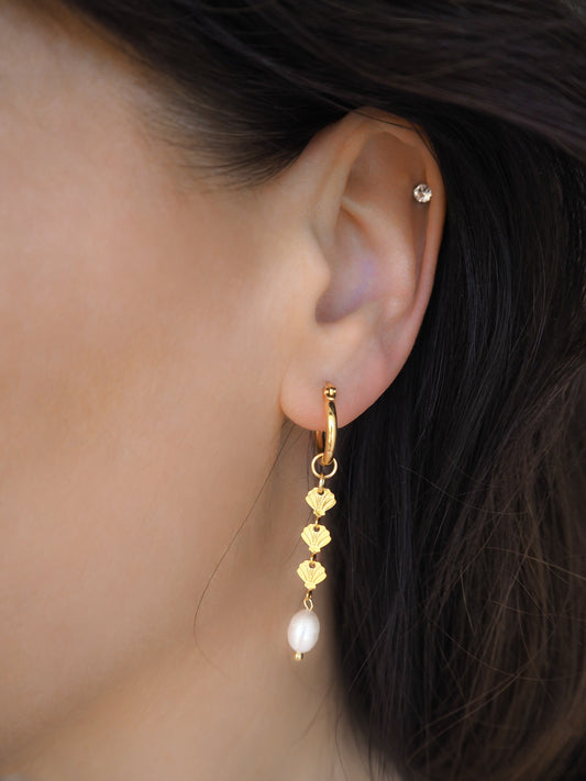 Model wearing gold hoop drop earrings with gold shells charms and freshwater pearl in ear. The earrings are made with 14k gold stainless steel and ivory white freshwater pearls. The three shell charms are tiny and detailed. 