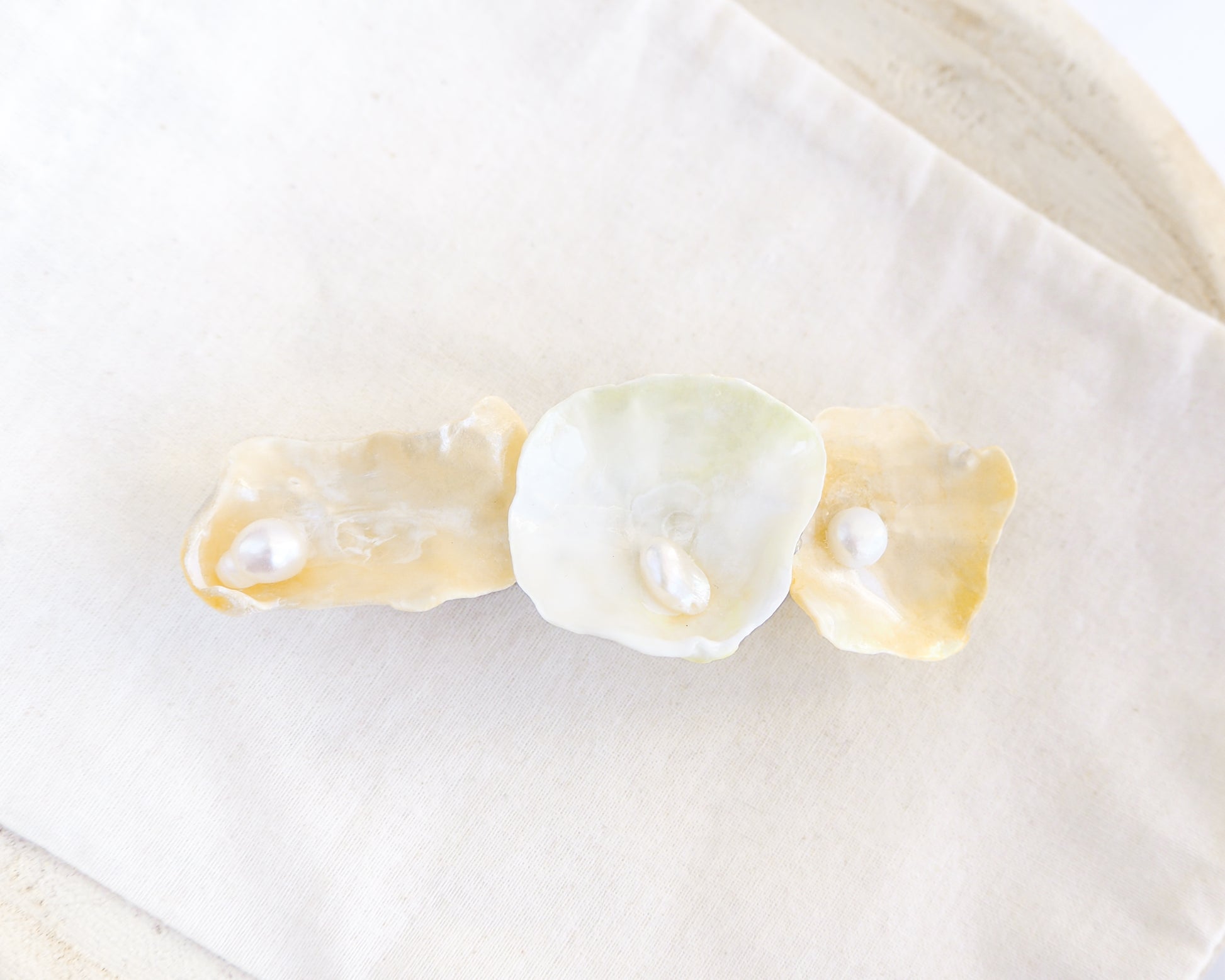Close up of pearl oyster shell hair clip on light cotton displayed. Made with handpicked jingle shells saddle oysters from Portugal. The hair clips has 3 shells with a soft yellow color. Jingle Shell Pearl Hair clip. Boho Seashell Beach Clip from Portugal, Handpicked Real Shells, Seashell Hair Decoration, Bohemian Seashell Wedding Hair accessories, Coastal Christmas gift, Beach Wedding Hair