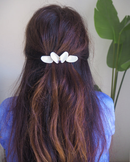 Person with long, wavy hair wearing a white butterfly hair clip against a neutral background. Model wearing White Coquina Shells Butterfly Hair Clip Barrette, Handpicked Real Coquina Shells. The shells are white in color and attached on the hair clip like a butterfly. The model has brown long hair. Sea Butterfly Shell Hair Decoration, Seashell Wedding Hair accessories, Coastal Christmas gift, Beach Wedding Hair