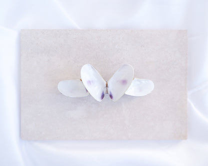 White Coquina Shells Butterfly Hair Clip Barrette on light stone displayed. Handpicked Real Coquina Shells. The shells are white in color and attached on the hair clip like a butterfly. The model has brown long hair. Sea Butterfly Shell Hair Decoration, Seashell Wedding Hair accessories, Coastal Christmas gift, Beach Wedding Hair