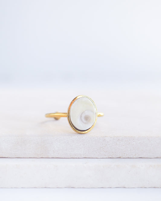 Gold bezel ring with a ivory shiva eye on stone displayed with light background. White Eye of Saint Lucia Gold Ring on stone displayed, 18k gold stainless steel shiva eye operculum, Saint Lucy Eye, operculum pendant