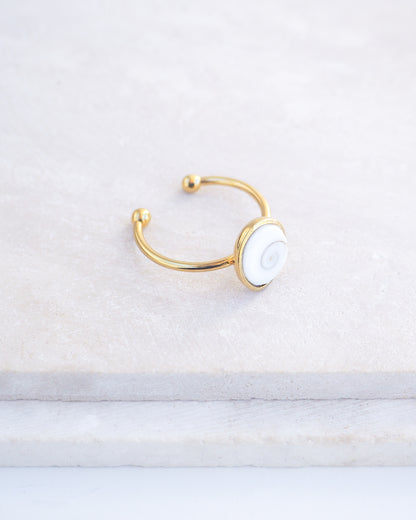 Side view of Gold bezel ring with a white shiva eye on stone displayed with light background. White Eye of Saint Lucia Gold Ring on stone displayed, 18k gold stainless steel shiva eye operculum, Saint Lucy Eye, operculum pendant