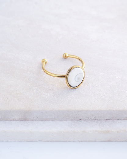 Side view of Gold bezel ring with a tiny ivory white shiva eye on stone displayed with light background. White Eye of Saint Lucia Gold Ring on stone displayed, 18k gold stainless steel shiva eye operculum, Saint Lucy Eye, operculum pendant