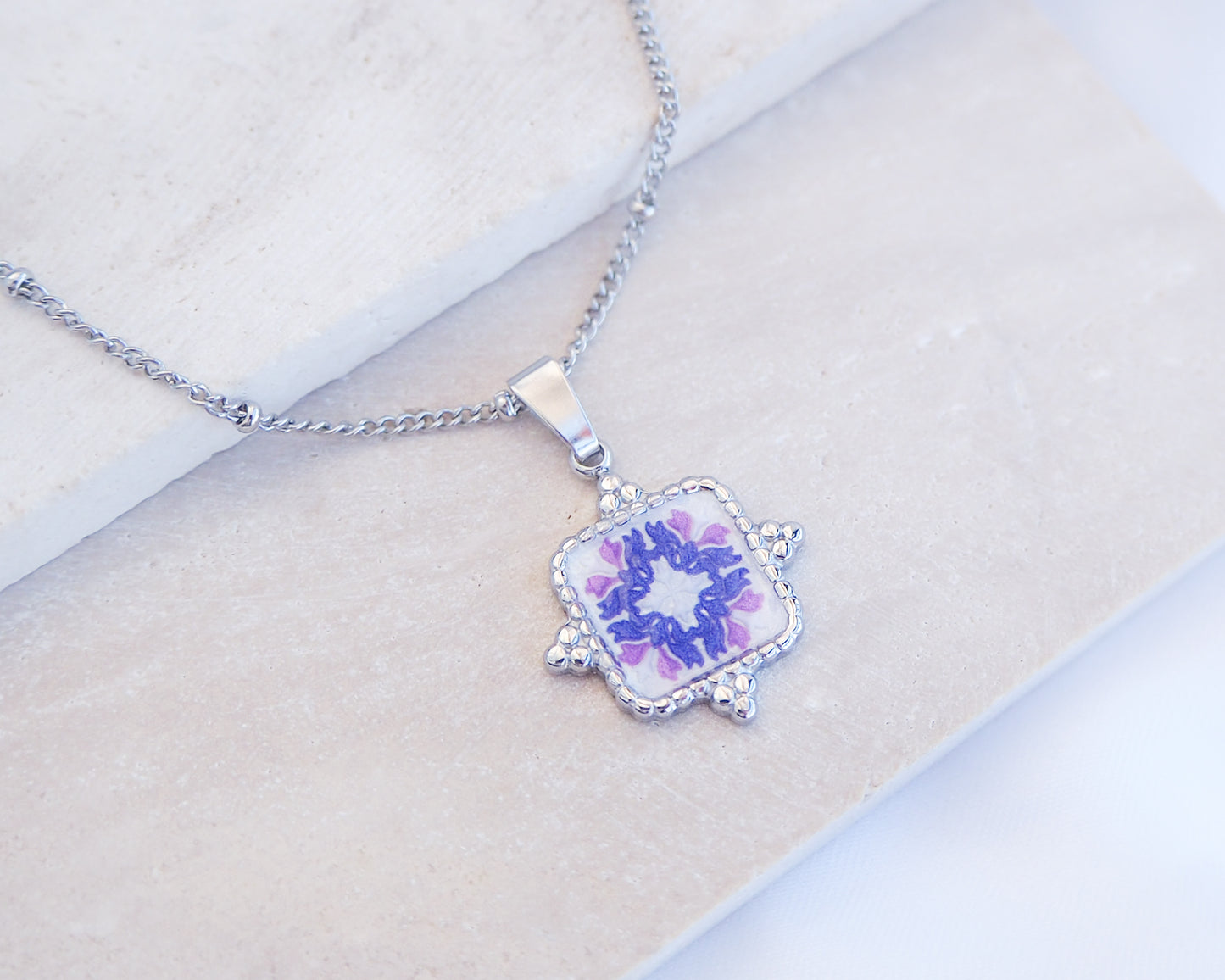 Close up of Purple Pink Portuguese Tile Square Necklaces Silver on stone displayed. Made with Silver stainless steel and white purple pink mosaic pendant inspired by the Portuguese Azulejo design pattern. 