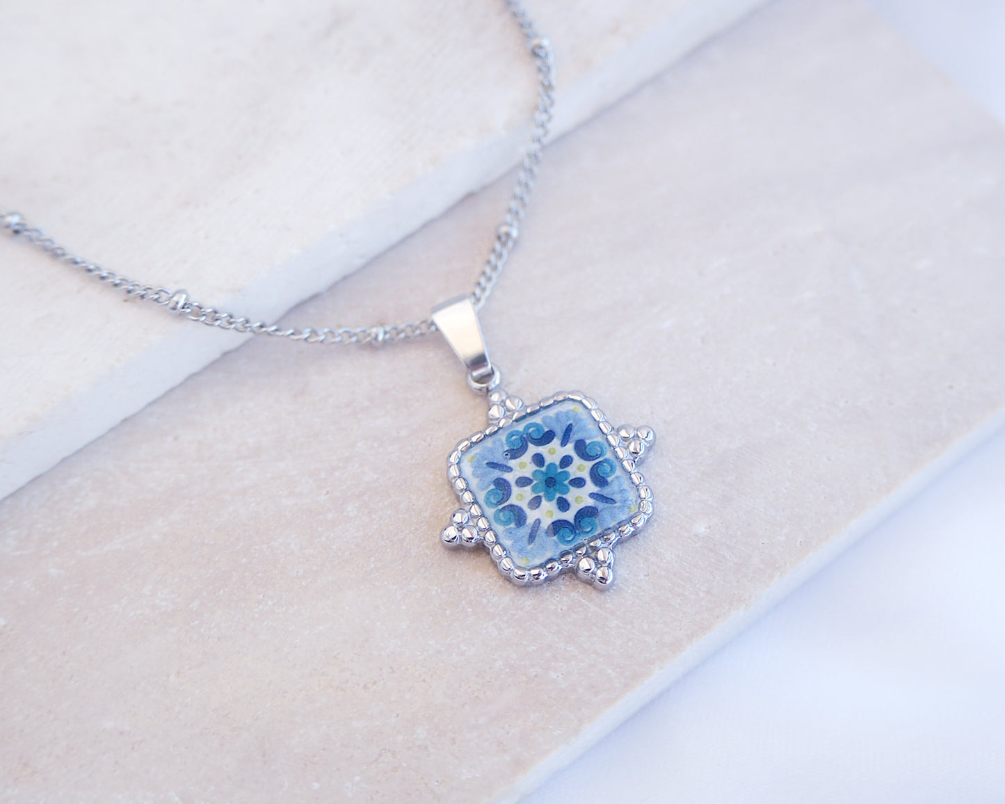 Close up of Blue Turquoise Portuguese Tile Square Necklaces Silver on stone displayed. Made with Silver stainless steel and white blue mosaic pendant inspired by the Portuguese Azulejo design pattern. 