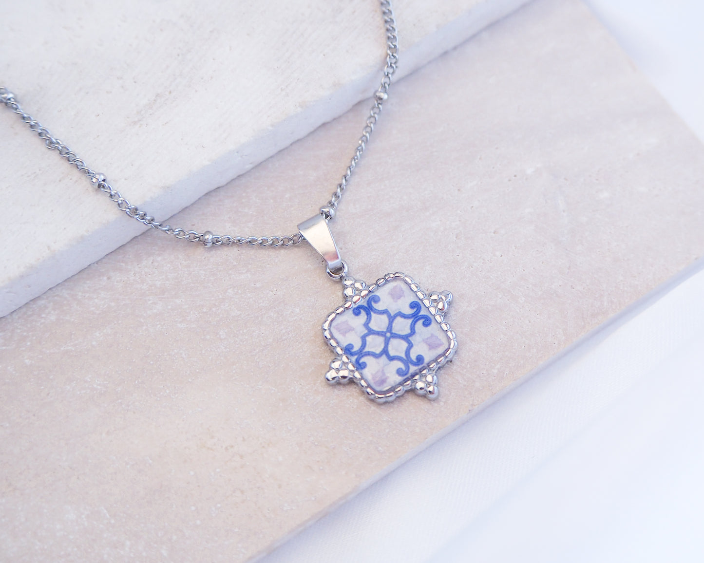 Close up of White Blue Portuguese Tile Square Necklaces Silver on stone displayed. Made with Silver stainless steel and white blue mosaic pendant inspired by the Portuguese Azulejo design pattern. 