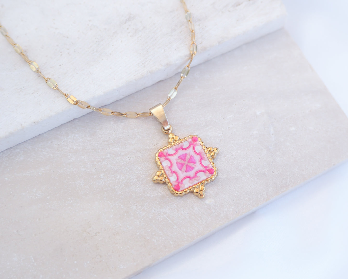 Close up of Pink White Portuguese Tile Square Necklaces Gold on stone displayed. Made with 18k gold stainless steel and white pink mosaic pendant inspired by the Portuguese Azulejo design pattern. 