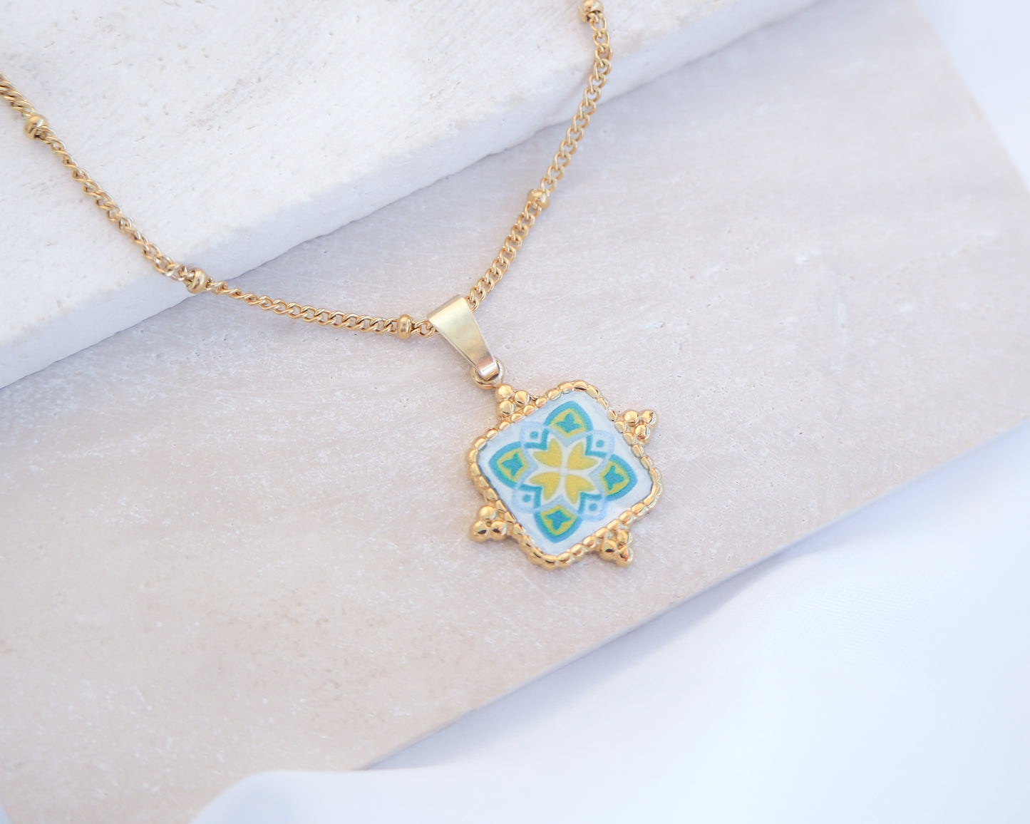 Close up of Green Yellow Portuguese Tile Square Necklaces Gold on stone displayed. Made with 18k gold stainless steel and white green yellow mosaic pendant inspired by the Portuguese Azulejo design pattern. 